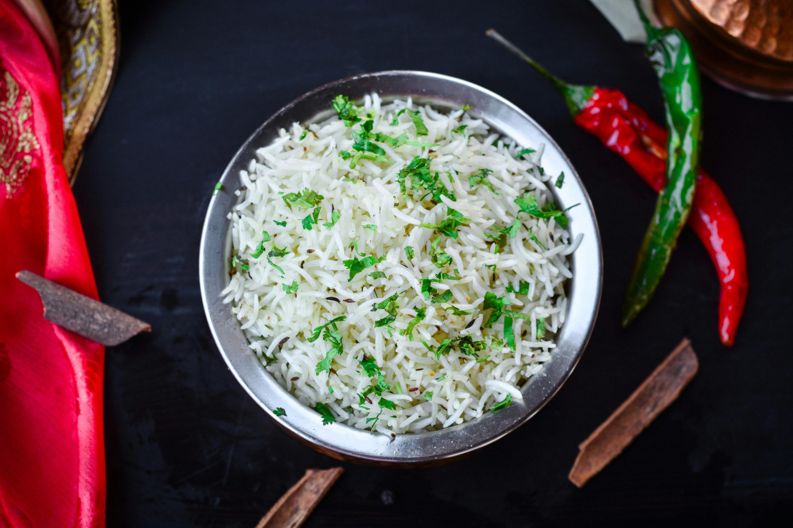 cooked basmati rice served in a stainless steel bowl with red and green chilis around it