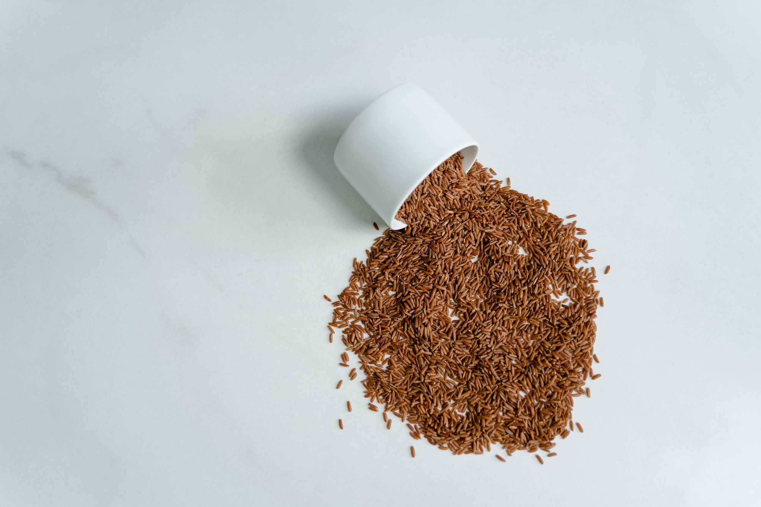 brown rice scattered on a surface beside a tipped-over bowl