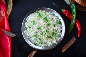 cooked basmati rice served in a stainless steel bowl with red and green chilis around it